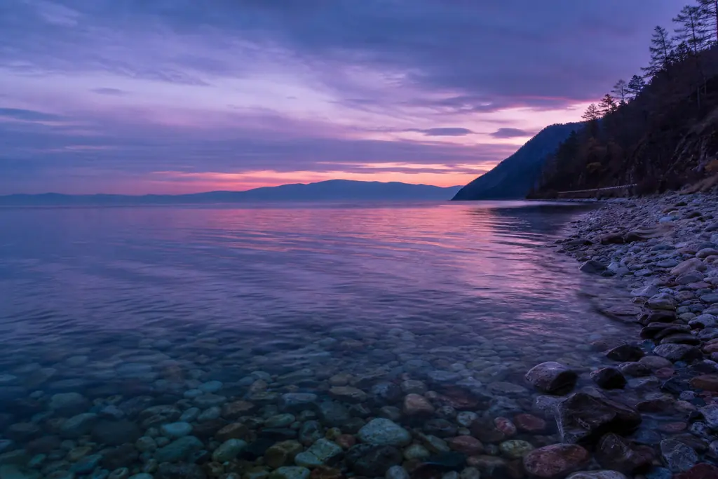 Orilla del lago Baikal con agua transparente y guijarros al atardecer (imagen generada con AI)