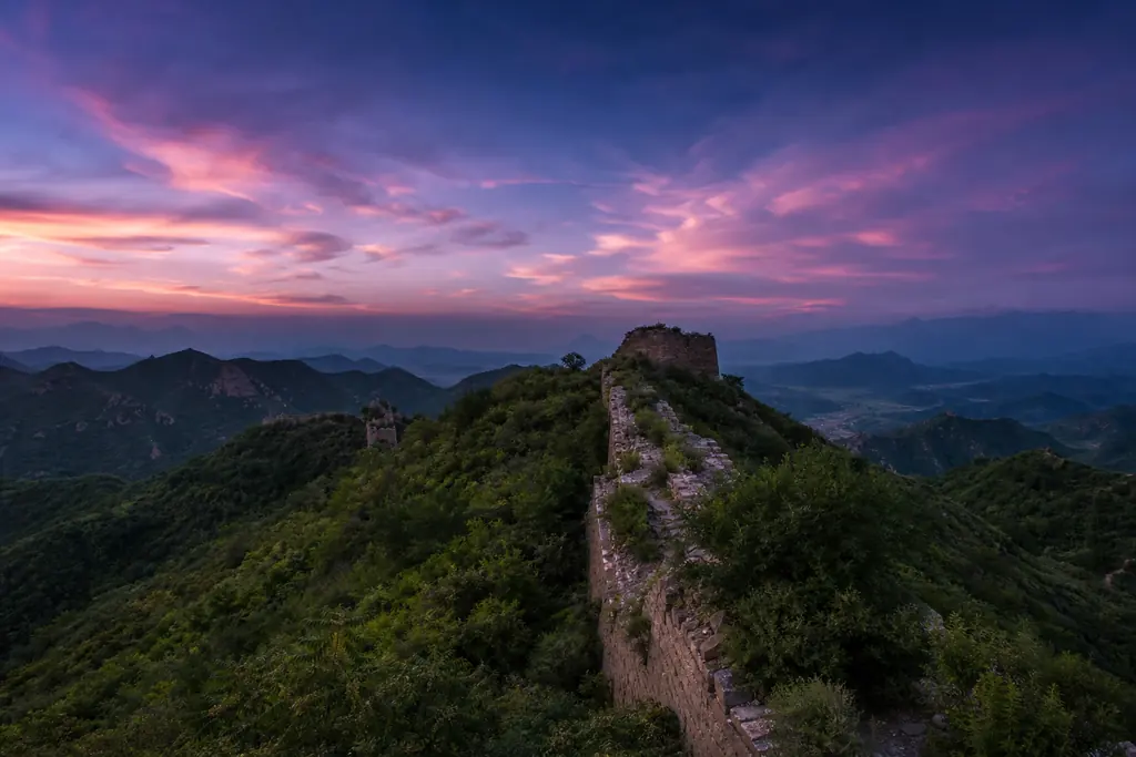 Tramo sin restaurar de la Gran Muralla entre colinas verdes al atardecer (imagen generada con AI)